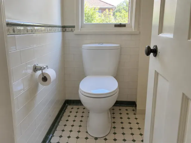Clean white toilet in a tiled bathroom with a window and patterned floor in Chatswood