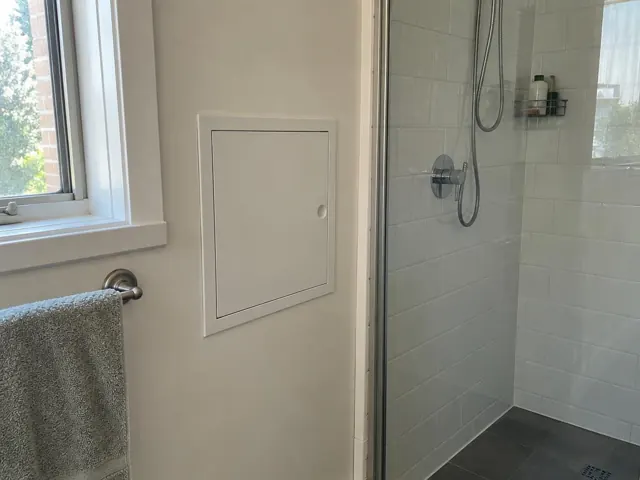 Small access panel in a tiled bathroom wall beside a shower and window in Killara
